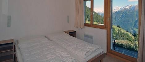 A bedroom with a bed, a nightstand, a window with a view of mountains, and a ceiling light.