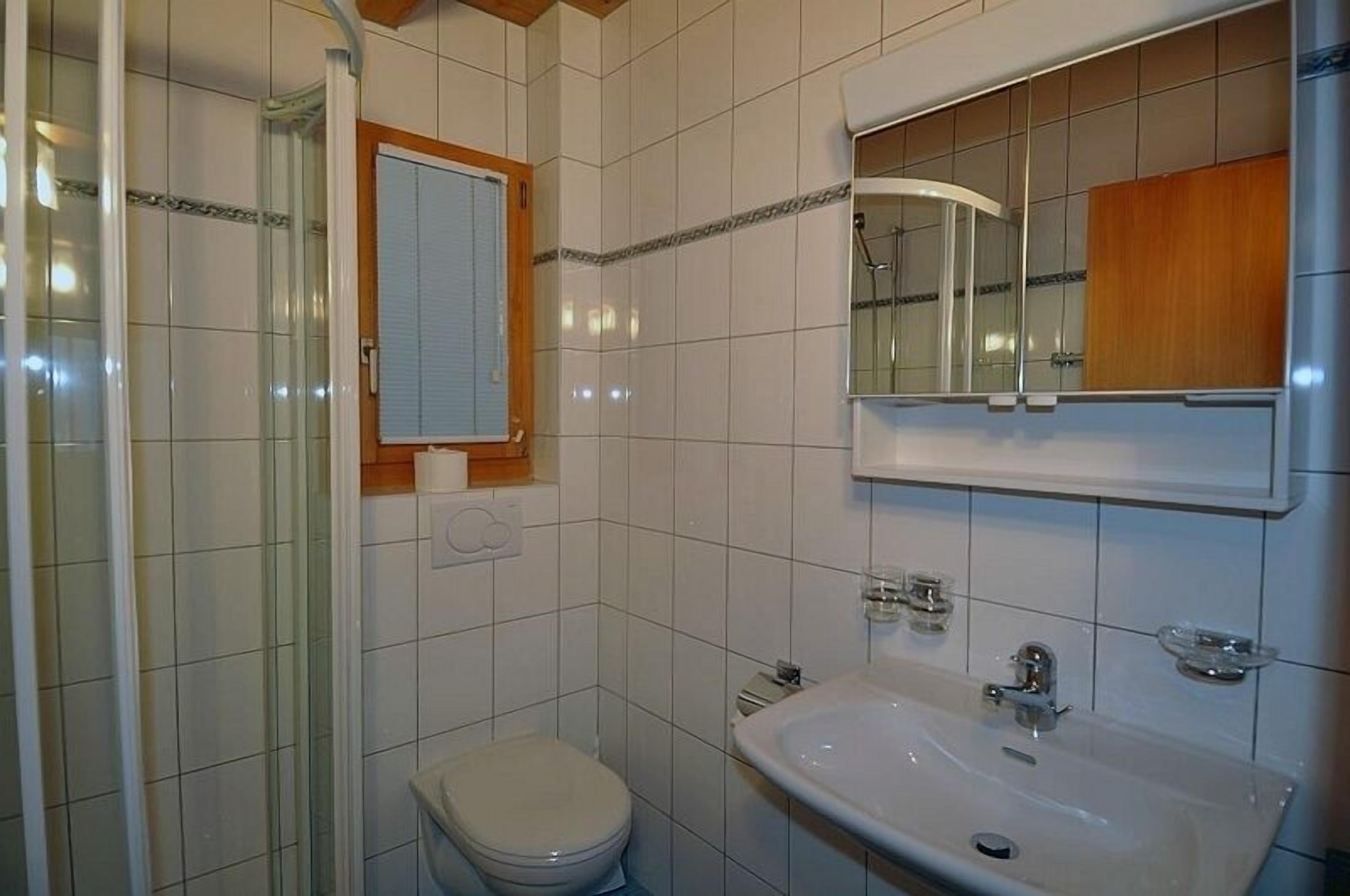 Un baño con inodoro, lavamanos, espejo y cabina de ducha.