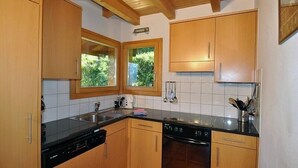 Een keuken met houten kastjes, een zwart aanrecht en een raam met uitzicht op groen.