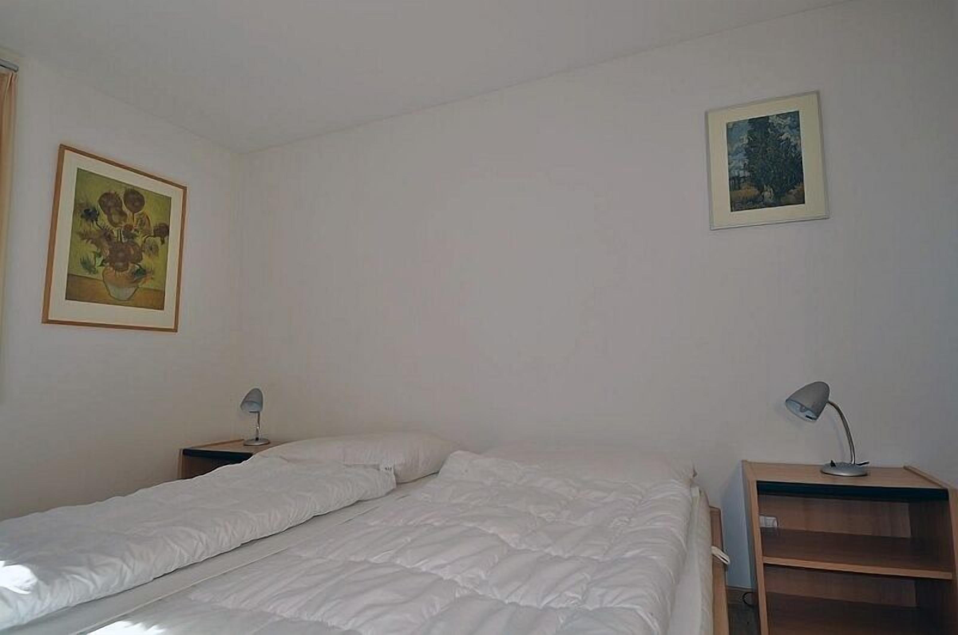 Et simpelt, rent værelse med en seng, to sengeborde og to billeder hængende på væggene.