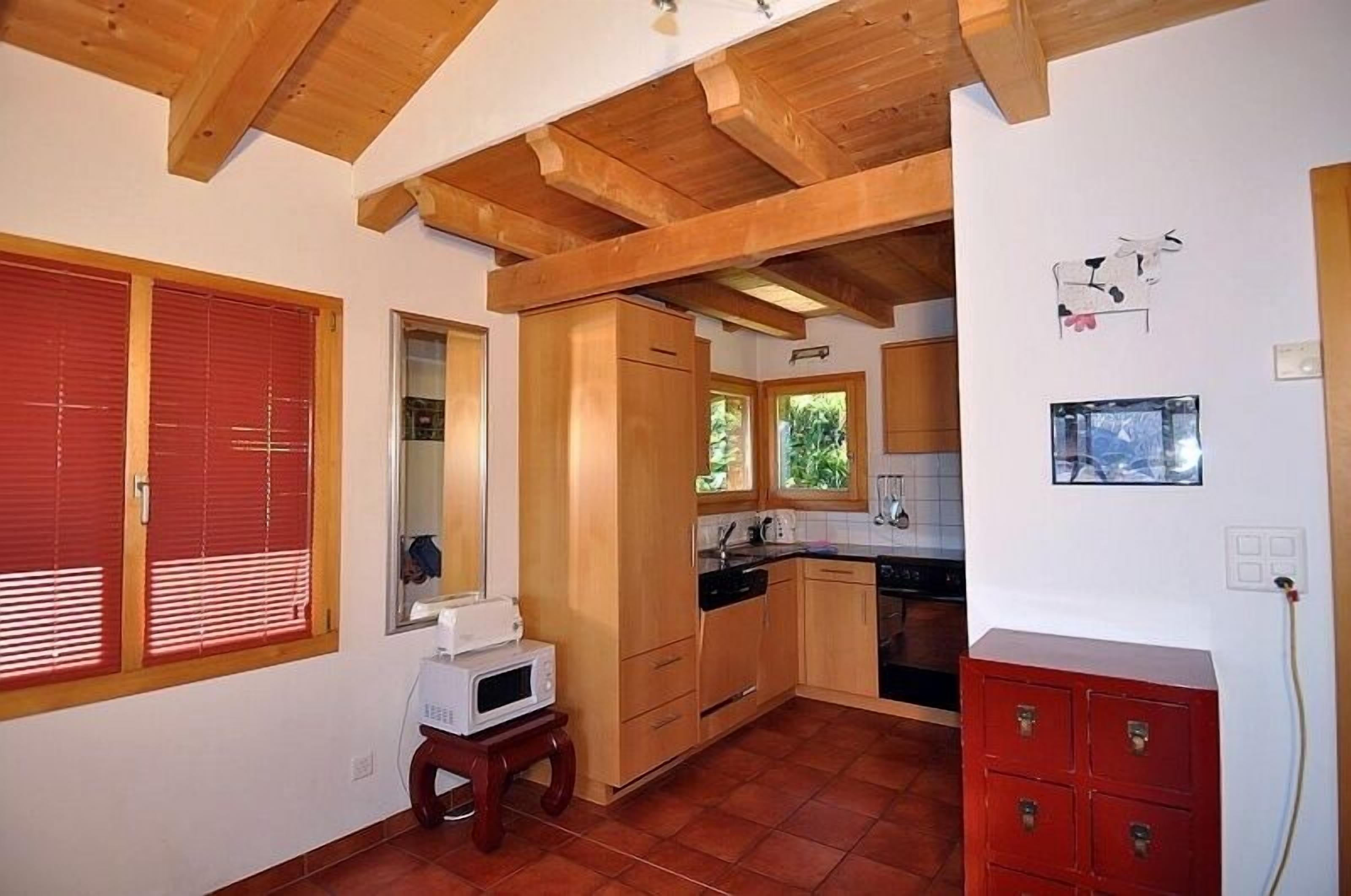 A kitchen with wooden cabinets, a red cabinet, a microwave, and a window with blinds.