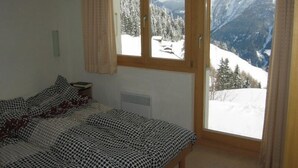 Een slaapkamer met een bed en een raam met uitzicht op besneeuwde bergen.
