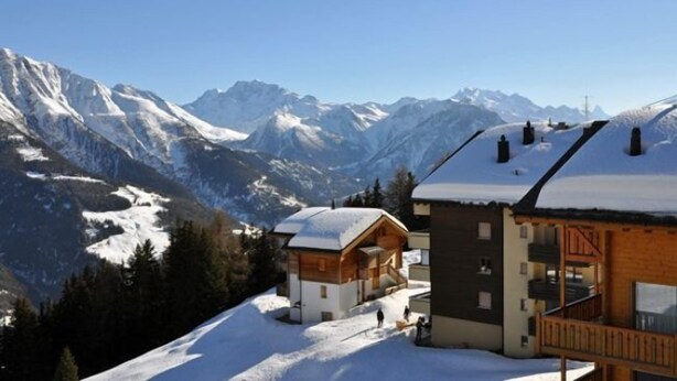 Eine Berglodge mit Holzhütten und einer Seilbahn, umgeben von schneebedeckten Berggipfeln.