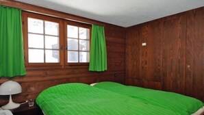 Ein Zimmer mit Holzwänden, einem Bett, einem Nachttisch, einer Lampe und einem Fenster mit Vorhängen.