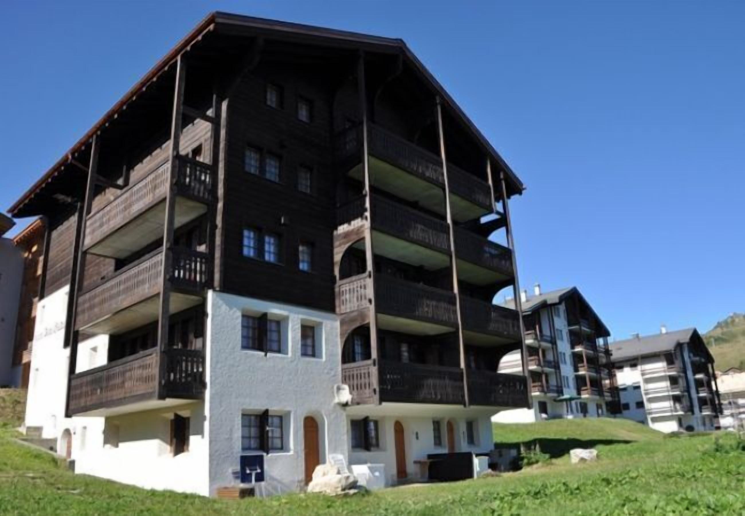 A multi-story building with balconies, a flat roof, and a hillside location.