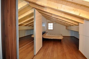 A bedroom with a sloped ceiling, wooden flooring, a bed, and a window. - Marjo OG (Ernen)