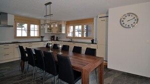 A modern kitchen with a wooden dining table, black chairs, and a clock on the wall. - Marjo OG (Ernen)