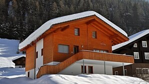 A wooden chalet with a balcony, surrounded by snow-covered landscape and forest. - Marjo EG (Ernen)