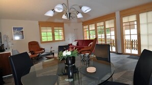 A modern dining area with a glass table, black chairs, a red sofa, and a ceiling light fixture. - Marjo EG (Ernen)