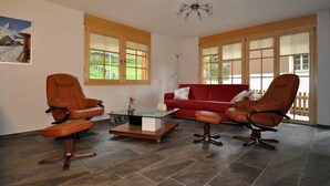 A living room with two brown leather chairs, a red sofa, and a glass coffee table. - Marjo EG (Ernen)