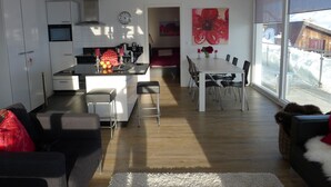 A modern kitchen with white cabinets, a central island, and a dining area with a white table and chairs. - Bella Vista (Fiesch)