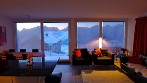 A modern living room with a dining area, large windows with mountain views, and a cozy seating arrangement. - Bella Vista (Fiesch)