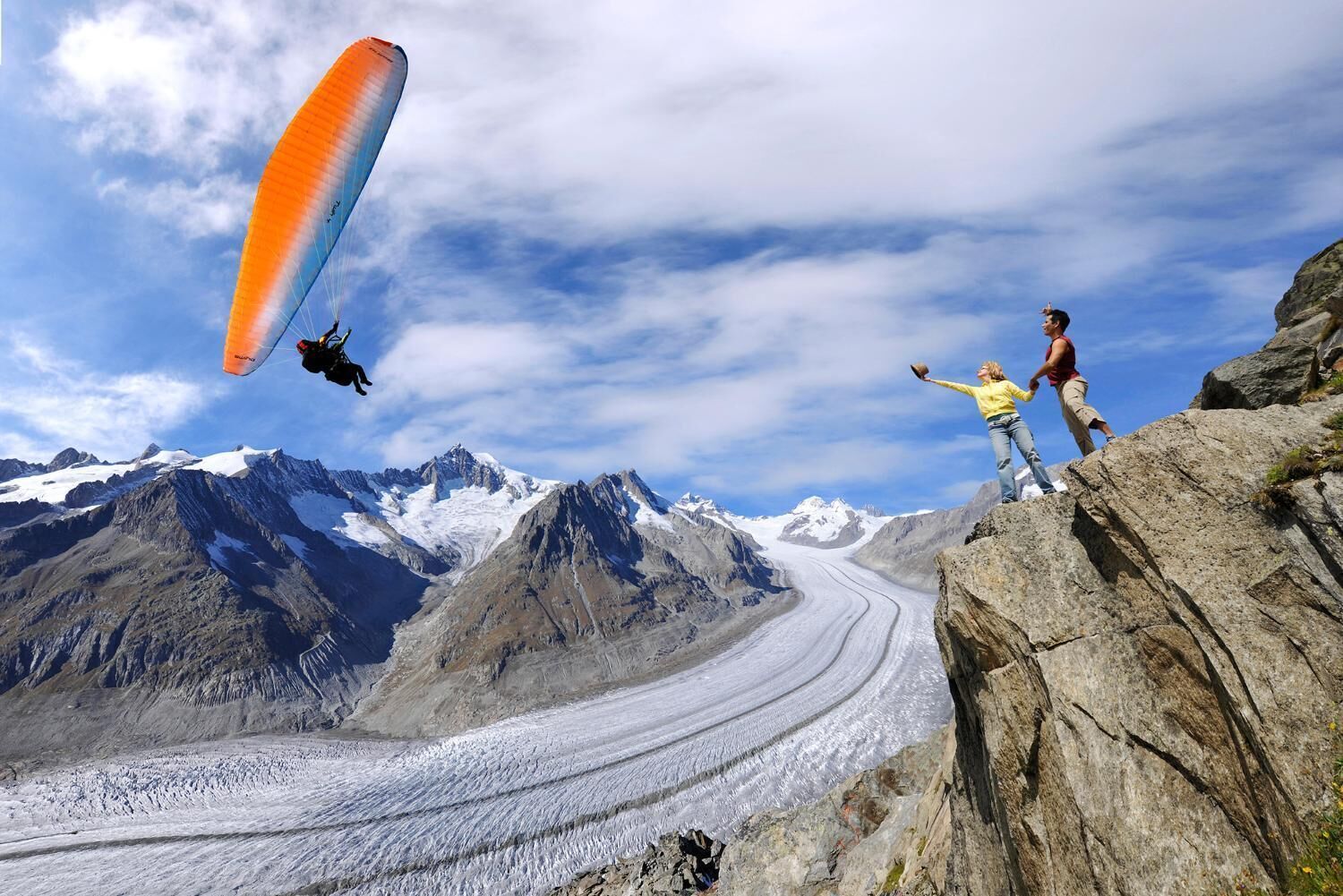 A person paragliding over a glacier with mountains in the background.