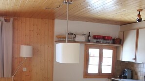 Une table de salle à manger en bois, avec six chaises, une lampe et un coin cuisine comprenant des placards et un évier.