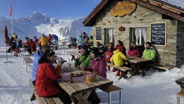 Un refuge de montagne en bois, appelé « Hort-Hitta », avec des murs en pierre et un panneau indiquant les plats proposés.