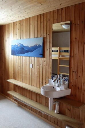 A wooden-paneled bathroom with a mounted picture of mountains, a sink, and a mirror.