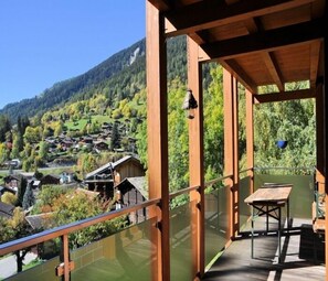 A wooden balcony with a glass railing overlooking a village nestled in a valley. - Aleid Sunshine (Fiesch)