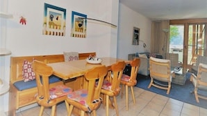 Un comedor con mesa y sillas de madera, un banco y vista al exterior a través de un ventanal.
