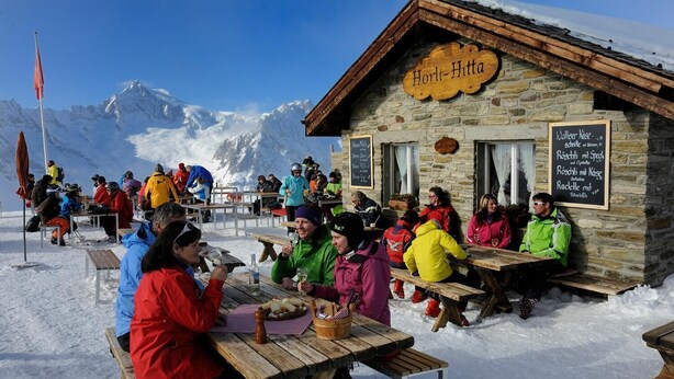 A stone building with a sign reading "Horli-Hitta" and outdoor seating for guests. - Carpe Diem 2 (Fiesch)