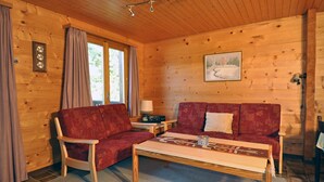 A cozy cabin with a wooden interior, featuring a sofa, a chair, a small table, and a lamp. - Carpe Diem 2 (Fiesch)