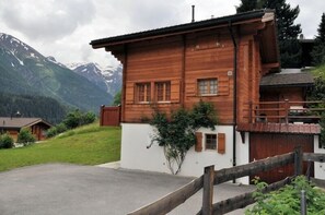 Una cabaña de madera con fachada blanca, ubicada frente a montañas.
