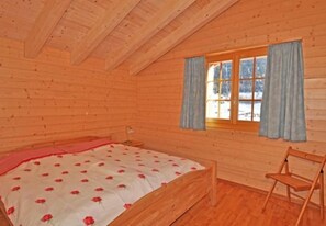 Una habitación tipo cabaña de madera con una cama, una ventana con cortinas y una silla.