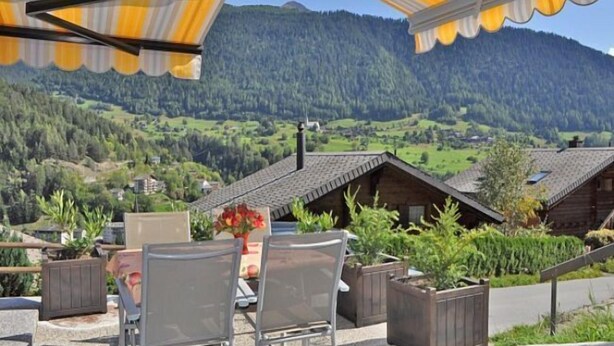 A terrace with chairs and a table, overlooking a mountainous landscape with houses. - De Hooghe Stee (Fiesch)