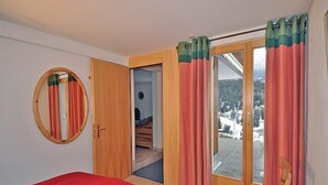 A bedroom with a bed, a wooden chair, a circular mirror, and a sliding glass door leading to a balcony. - De Hooghe Stee (Fiesch)