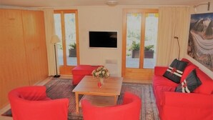A living room with red furniture, a flat-screen TV, and a painting on the wall. - De Hooghe Stee (Fiesch)