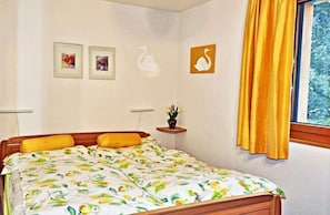 A bedroom with a bed, a window with yellow curtains, and wall art including swan silhouettes and framed pictures. - Dorothy Sunshine (Fiesch)