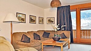 Una sala de estar acogedora con un sofá, una mesa con un florero y una lámpara. Hay cuadros en la pared y se ve un paisaje nevado a través de una ventana.