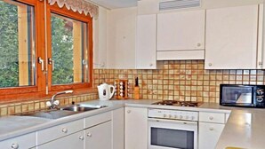 Una cocina compacta con ventana, armarios blancos, estufa y microondas.