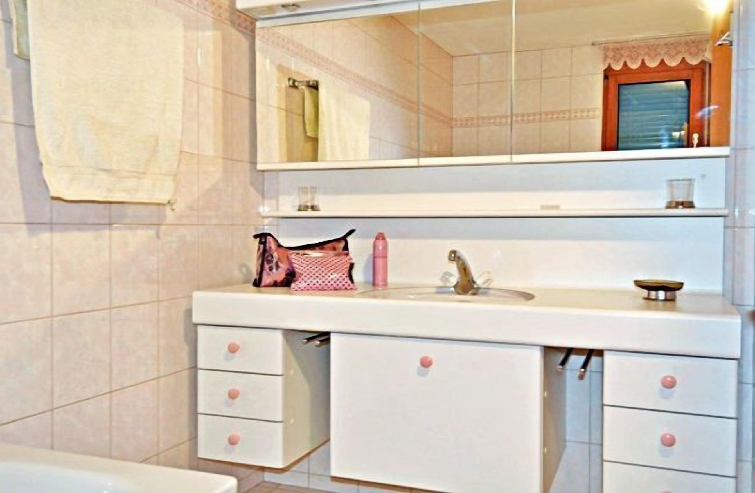 Un baño con lavamanos blanco, espejo y dos cajones.