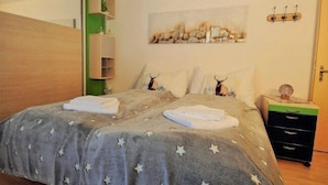 A bedroom with a bed, a nightstand, a green shelving unit, and a wall-mounted artwork. - Edelweiss Eden (Fiesch)