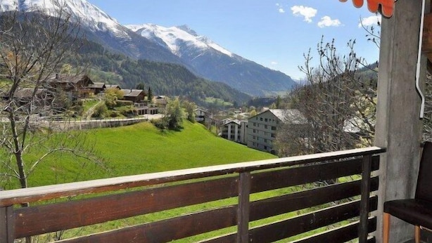 A balcony with a wooden railing overlooking a mountainous landscape with snow-capped peaks and a green valley. - Edelweiss Eden (Fiesch)