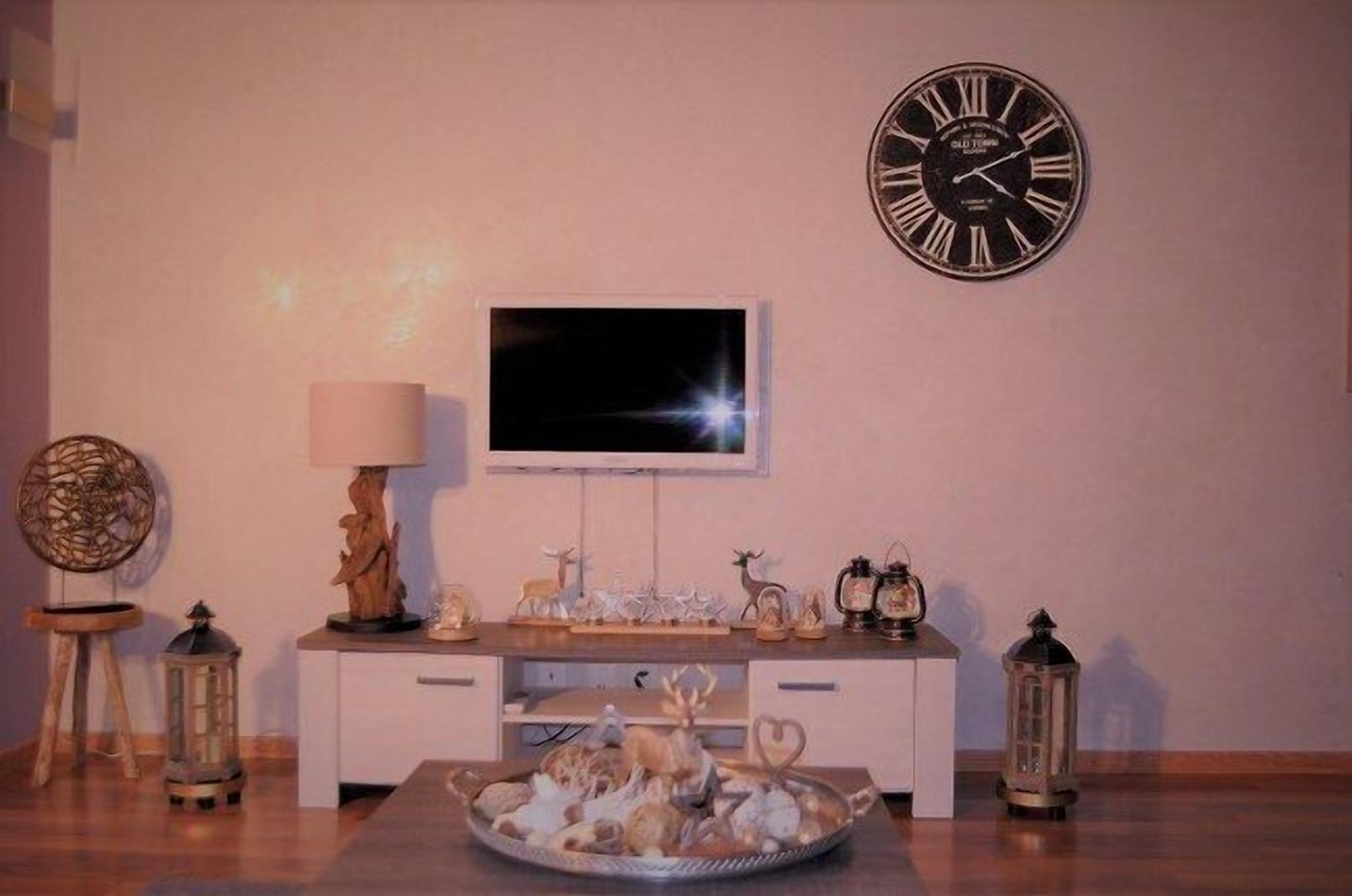 A living room with a white entertainment unit, a flat-screen TV, decorative items, and a clock on the wall.