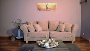 A living room with a beige sofa, a coffee table with decorative items, a vase with dried flowers, and a painting on the wall. - Edelweiss Eden (Fiesch)