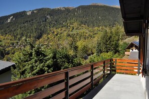 Ein Balkon mit Holzgeländer, der auf eine gebirgige Landschaft mit dichtem Wald und verstreuten Häusern blickt.