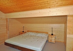 A small, wooden-paneled room with a single bed, two bedside tables, and a small dresser. - Lotus OG (Fiesch)