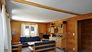 Une pièce confortable, aménagée comme un chalet, avec un canapé, un banc en bois, une télévision et un meuble contenant divers objets.