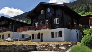 Un chalet à deux étages doté d’un balcon, de fondations en pierre et surplombant un paysage montagneux.