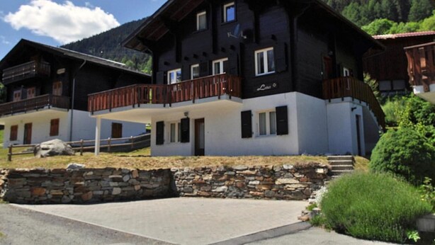 Un chalet à deux étages doté d’un balcon, de fondations en pierre et surplombant un paysage montagneux.
