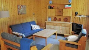Une pièce aux murs lambrés, avec un canapé bleu, une table en bois, un téléviseur et une bibliothèque.