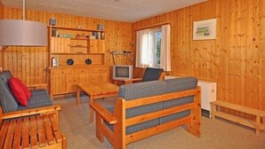L’intérieur d’un chalet en bois chaleureux et accueillant, avec un canapé, une petite table, un téléviseur et une fenêtre avec des rideaux.