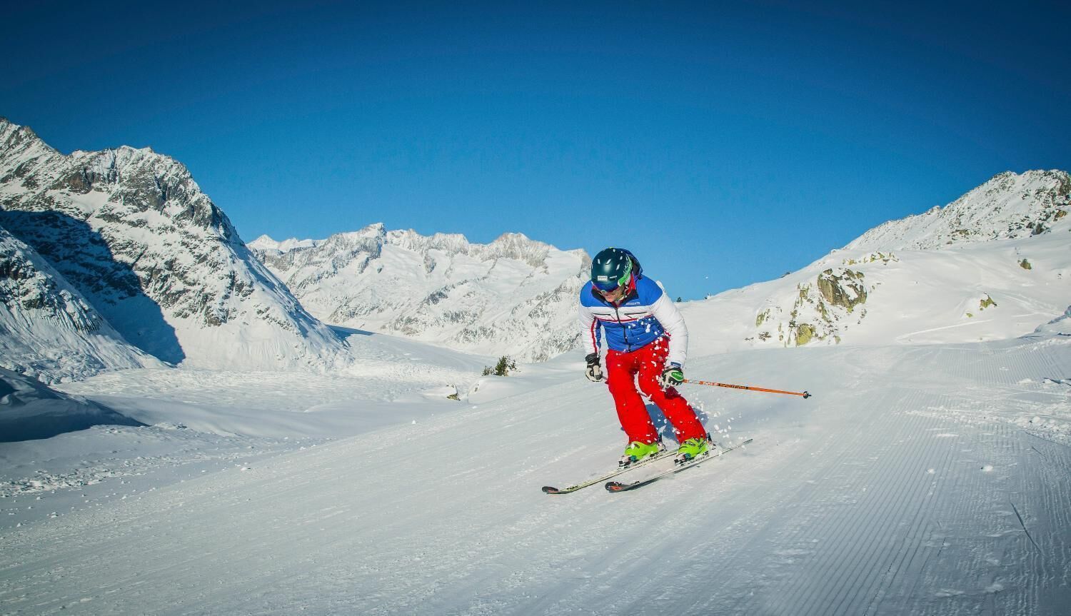 A skier on a snowy slope with mountains in the background.