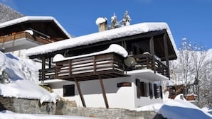 A chalet-style building with a wooden balcony and snow-covered roof, surrounded by snow. - Melchior (Fiesch)