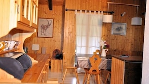 A cozy wooden cabin interior with a dining area, a bed with a canopy, and a small kitchen. - Melchior (Fiesch)