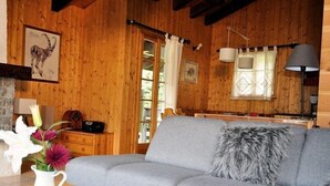 A cozy room with a grey sofa, wooden walls, a white pitcher with flowers, and a wooden cabinet. - Melchior (Fiesch)
