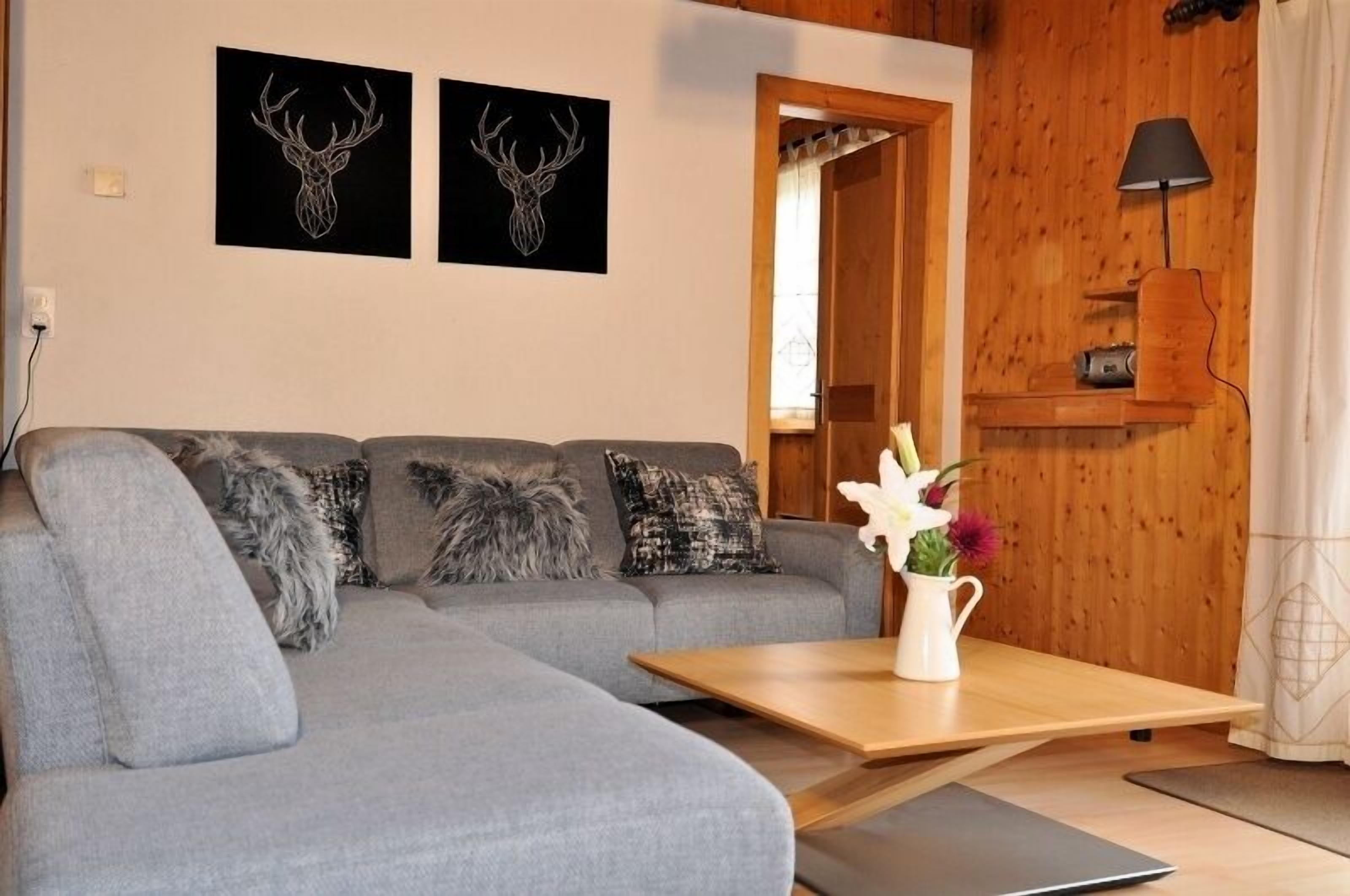 A modern living room with a grey sofa, two deer head wall art, a wooden coffee table, and a lamp.