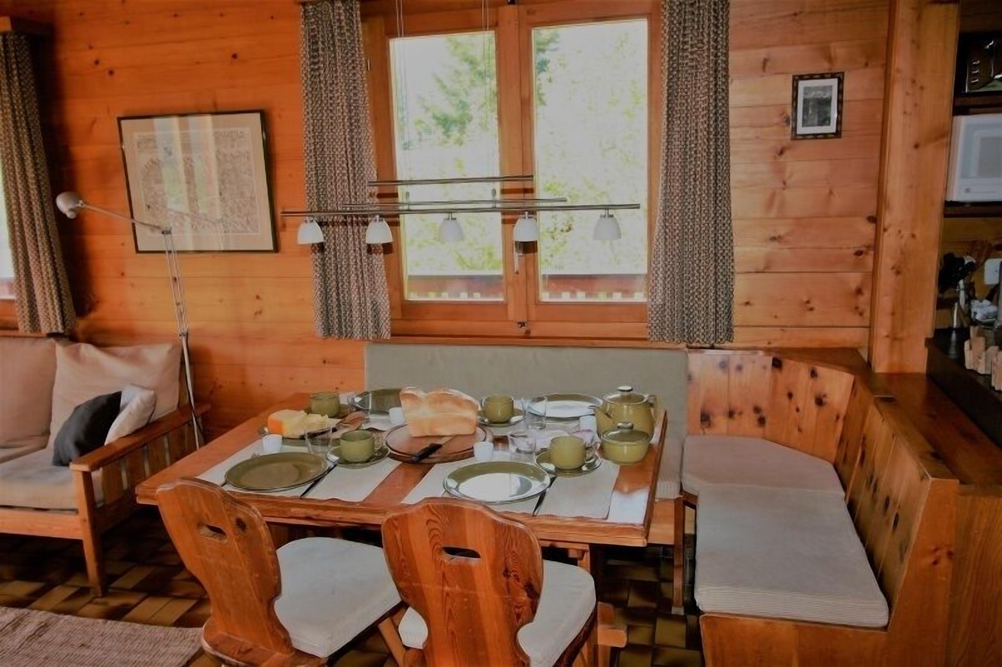 Une cabane en bois avec une table à manger dressée pour quatre personnes, deux bancs en bois et un canapé.
